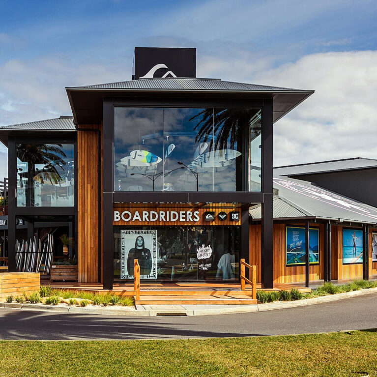 This vibrant exterior highlights the open, surf-inspired design. A glass façade frames suspended surfboards, while warm timber cladding complements the coastal surroundings. The inviting deck and detailed storefront underscore the space’s dual role as retail and community-focused.