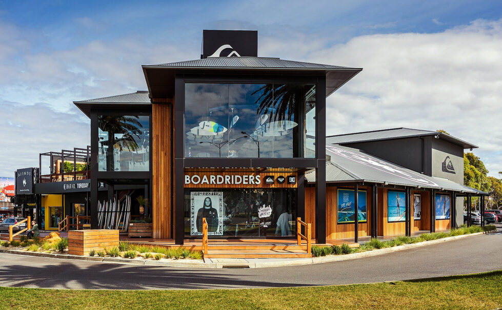 This vibrant exterior highlights the open, surf-inspired design. A glass façade frames suspended surfboards, while warm timber cladding complements the coastal surroundings. The inviting deck and detailed storefront underscore the space’s dual role as retail and community-focused.