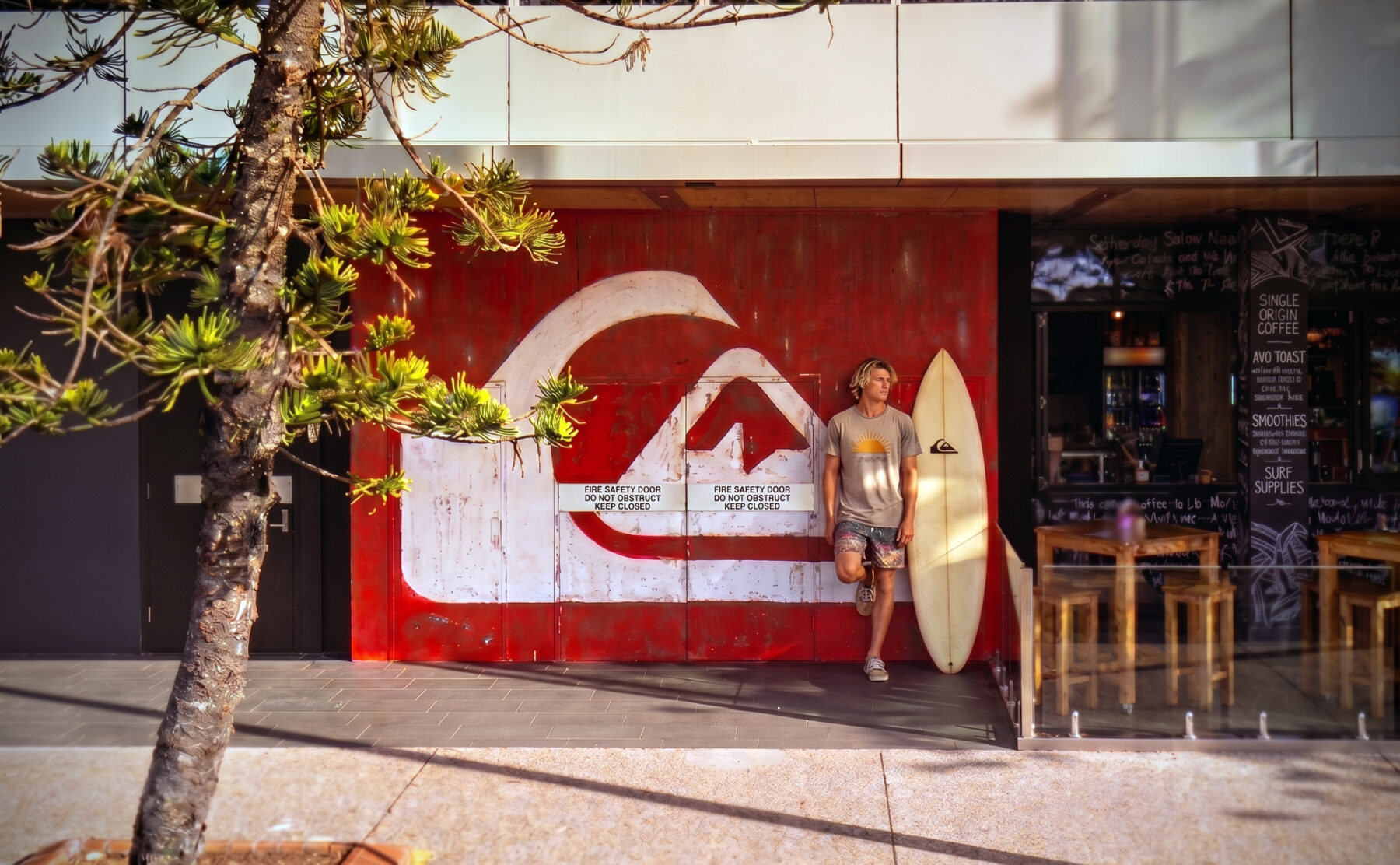 Commercial timber cladding, distressed wall mural, oversized branding logo, outdoor café seating, timber dining stools, concrete pavement, exterior glass balustrade.