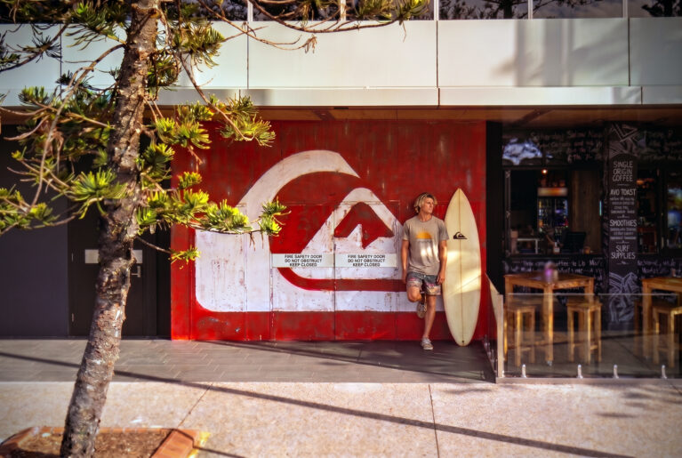 Commercial timber cladding, distressed wall mural, oversized branding logo, outdoor café seating, timber dining stools, concrete pavement, exterior glass balustrade.