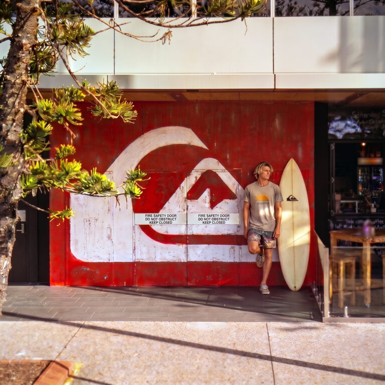 Commercial timber cladding, distressed wall mural, oversized branding logo, outdoor café seating, timber dining stools, concrete pavement, exterior glass balustrade.
