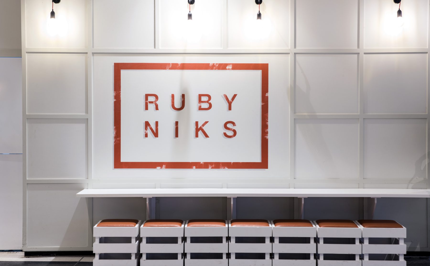 Grid wall paneling, modular crate stools, cantilevered bench table, kids cafe branding, minimalist cafe seating, wall mounted sconce lights, stenciled retail logo.
