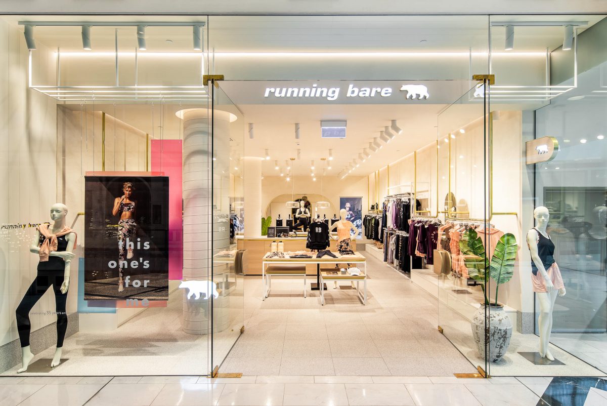 A full-height frameless glass facade with illuminated white signage and brass hinges.