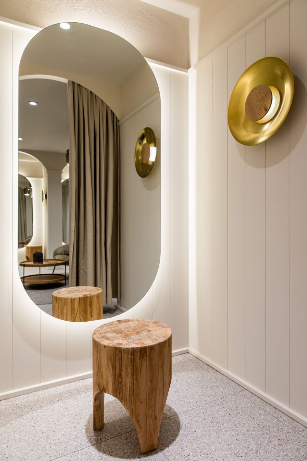 amazing backlighted mirror in a cosy and welcoming fitting room with terrazzo flooring, brass lighting and timber panelling on the walls. Interior design by design clarity