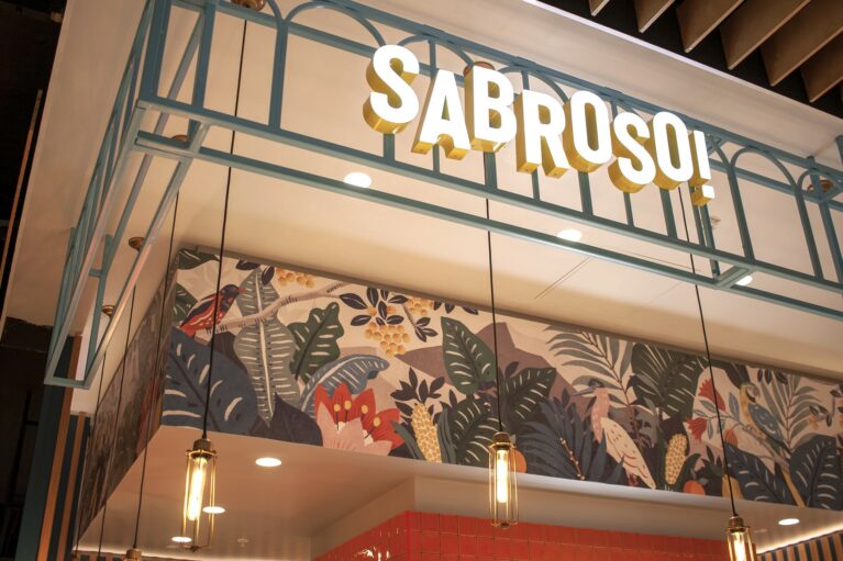 Illuminated 3D branding mounted on a light blue metal gantry structure.