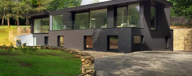 Skyridge’s exterior features sleek black timber cladding, blending seamlessly with its Surrey Hills setting. The design emphasizes subtle elegance and environmental harmony, with its dark facade and glass accents framing views of the surrounding countryside.