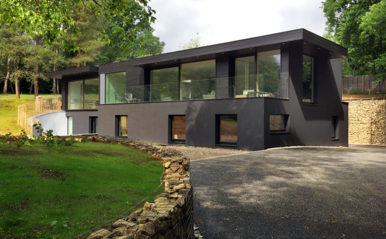Skyridge’s exterior features sleek black timber cladding, blending seamlessly with its Surrey Hills setting. The design emphasizes subtle elegance and environmental harmony, with its dark facade and glass accents framing views of the surrounding countryside.