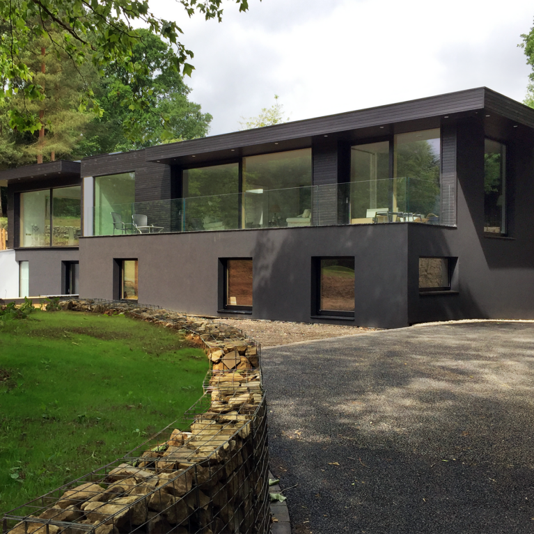 Skyridge’s exterior features sleek black timber cladding, blending seamlessly with its Surrey Hills setting. The design emphasizes subtle elegance and environmental harmony, with its dark facade and glass accents framing views of the surrounding countryside.