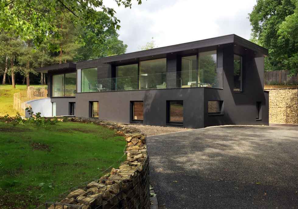 Skyridge’s exterior features sleek black timber cladding, blending seamlessly with its Surrey Hills setting. The design emphasizes subtle elegance and environmental harmony, with its dark facade and glass accents framing views of the surrounding countryside.