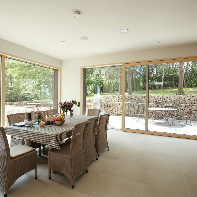 The dining area opens to panoramic views, with neutral tones and minimalist furnishings creating a calm, inviting space. Floor-to-ceiling windows frame the landscape, merging indoor and outdoor atmospheres for a seamless dining experience.