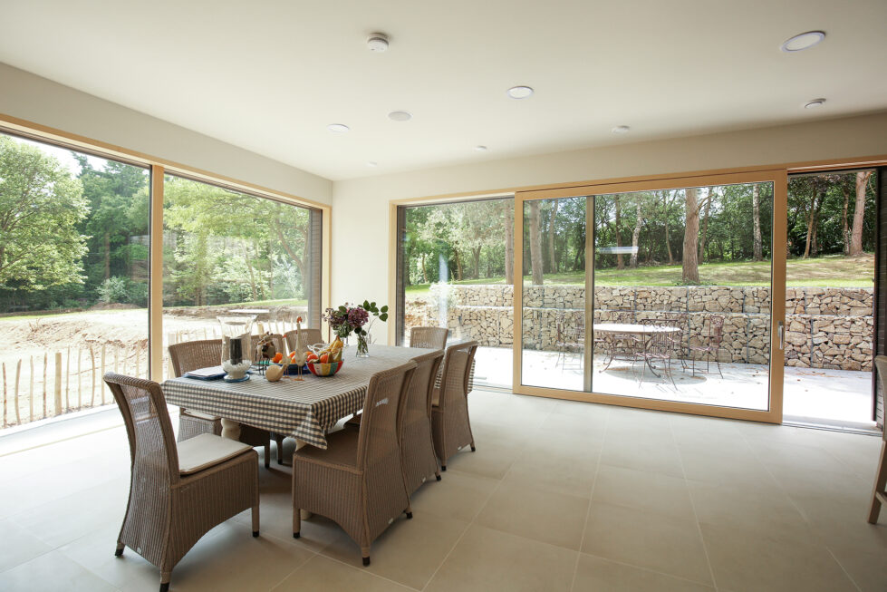 The dining area opens to panoramic views, with neutral tones and minimalist furnishings creating a calm, inviting space. Floor-to-ceiling windows frame the landscape, merging indoor and outdoor atmospheres for a seamless dining experience.