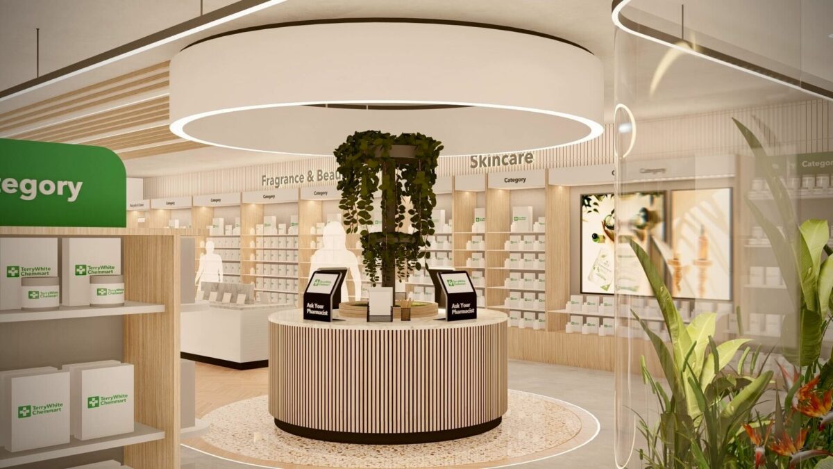 A circular pharmacist advice station anchored by cascading greenery beneath a sculptural ceiling light, providing a calm focal point within the skincare and fragrance area of the store.
