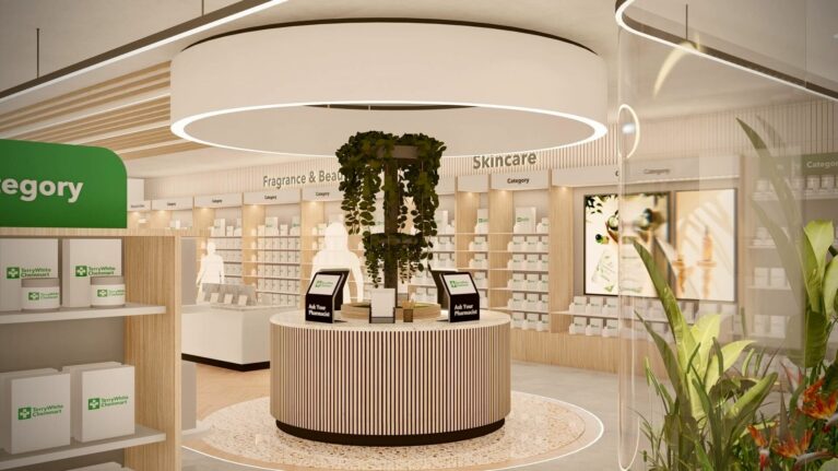 A circular pharmacist advice station anchored by cascading greenery beneath a sculptural ceiling light, providing a calm focal point within the skincare and fragrance area of the store.