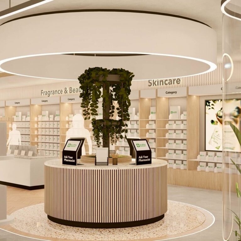 A circular pharmacist advice station anchored by cascading greenery beneath a sculptural ceiling light, providing a calm focal point within the skincare and fragrance area of the store.