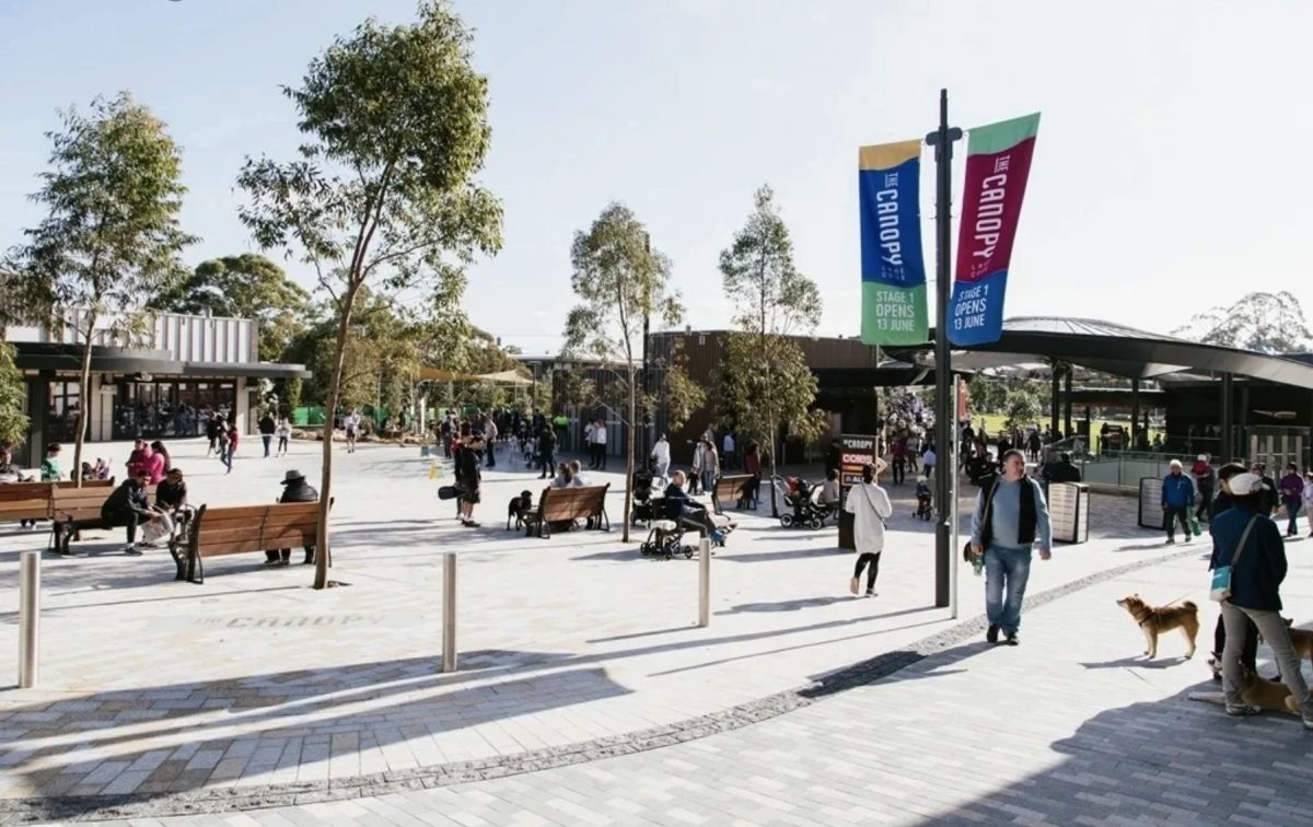 A bustling public plaza with modern architecture, ample seating, and shaded areas, creating a lively urban gathering spot.