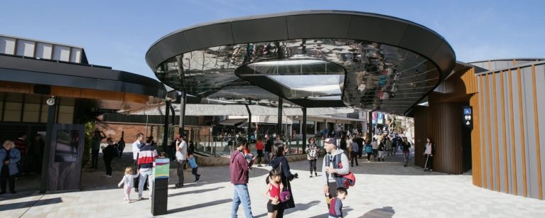 A modern metal canopy welcomes visitors to an open-air plaza, featuring sleek architectural lines and a bright, spacious design.