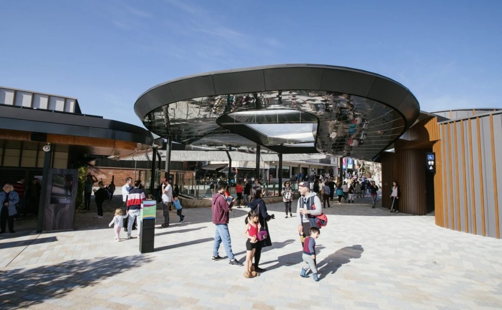 A modern metal canopy welcomes visitors to an open-air plaza, featuring sleek architectural lines and a bright, spacious design.