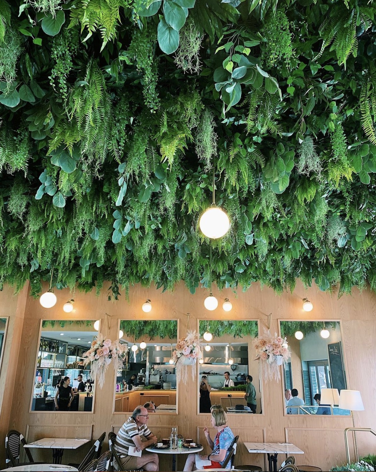 A lush, green ceiling canopy creates a natural ambiance in the cafe, complemented by soft floral accents and warm lighting.