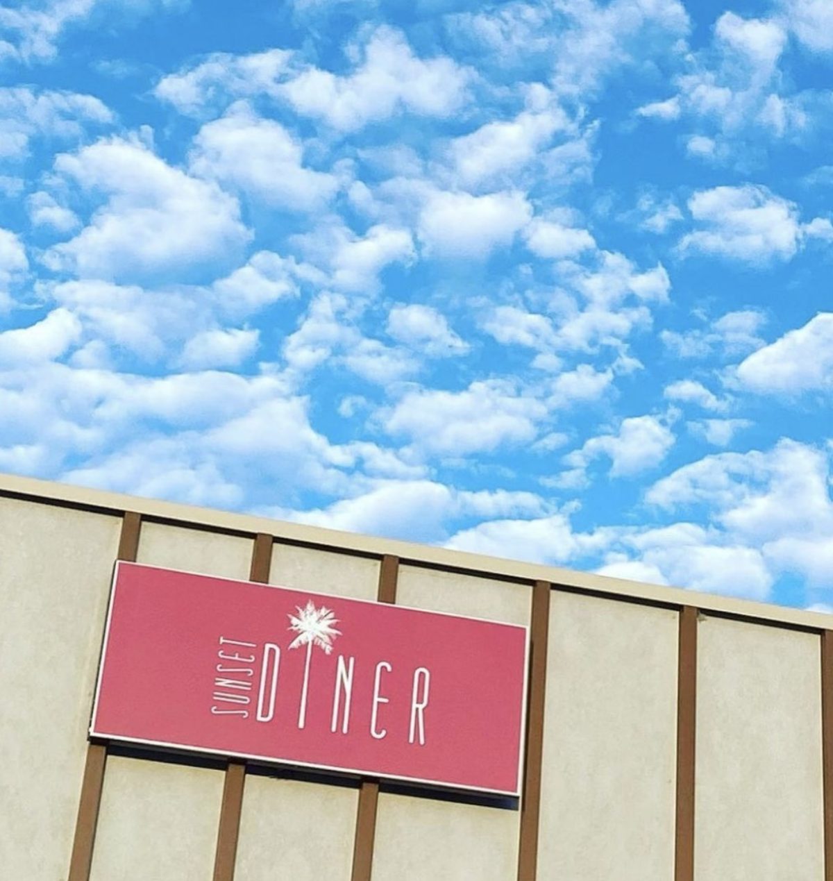 The Sunset Diner facade, featuring a bold pink sign with classic lettering and a palm tree graphic against a light beige exterior.