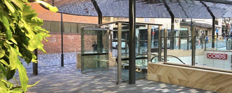 The Scott Carver plaza with escalator access, featuring modern paving, greenery, and a sleek canopy.