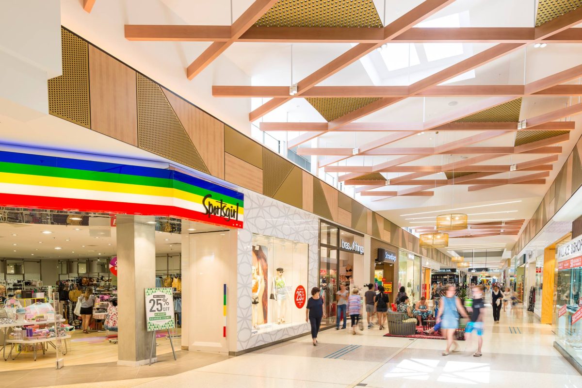 Retail mall arcade, timber ceiling baffles, skylight architecture, storefront design, polished stone flooring, glass facades, linear lighting, bulkhead panels.