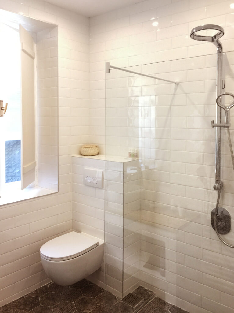 A sleek bathroom with a modern walk-in shower, clean white subway tiles, and luxurious finishes. Encaustic tiles and the Methven Aurajet Aio showerhead add artisanal charm and contemporary functionality.