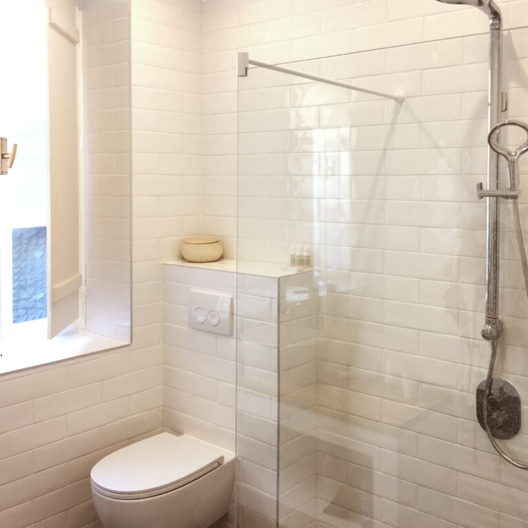 A sleek bathroom with a modern walk-in shower, clean white subway tiles, and luxurious finishes. Encaustic tiles and the Methven Aurajet Aio showerhead add artisanal charm and contemporary functionality.