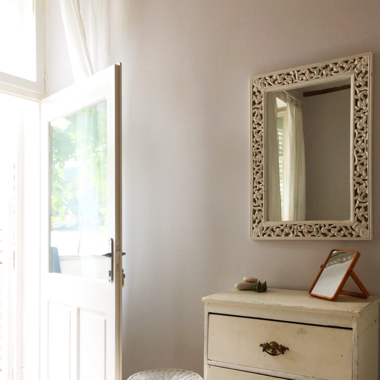 An elegant corner with vintage-inspired furnishings and modern simplicity. Carved wooden accents and light curtains frame a serene and functional space.