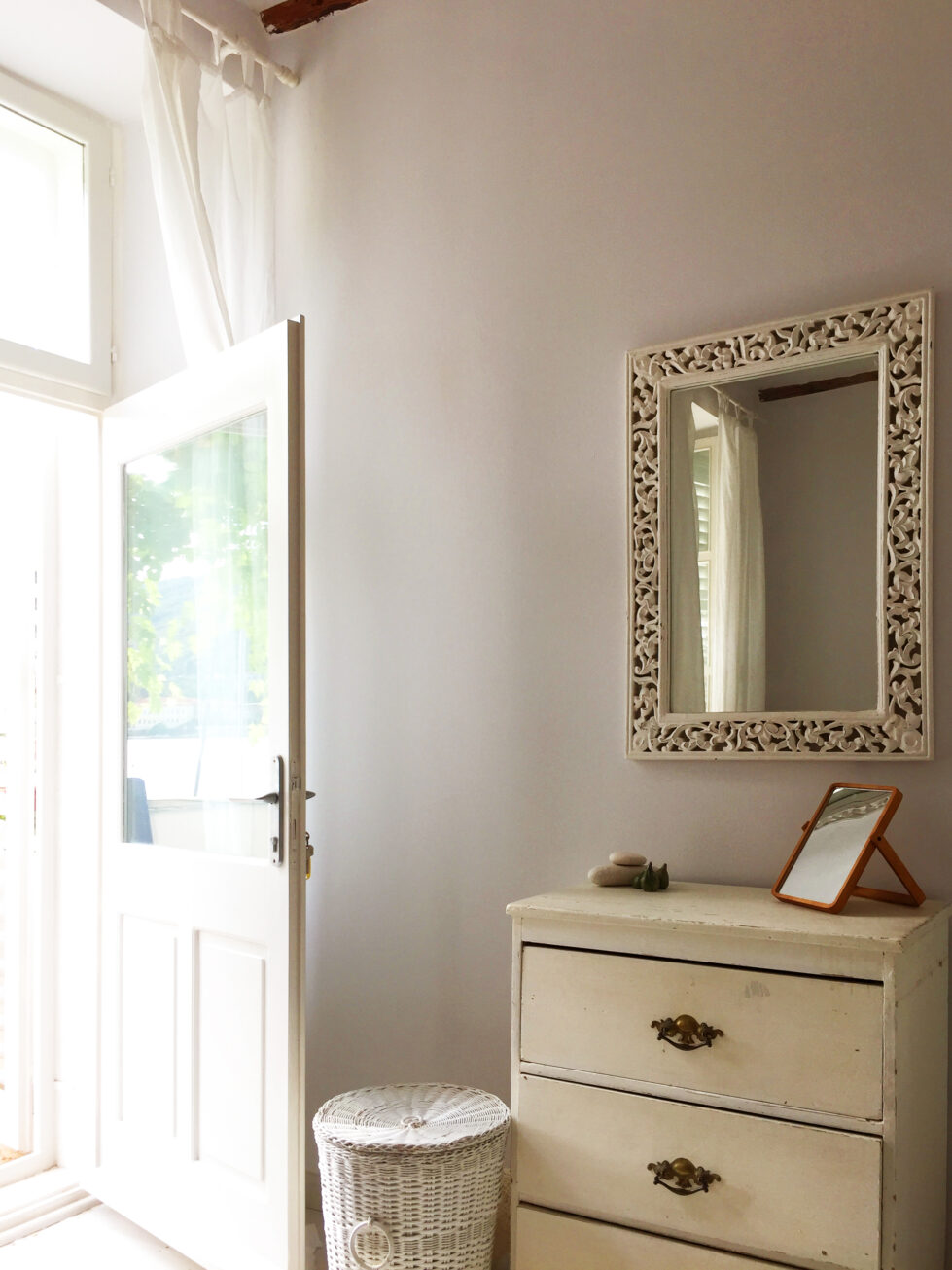 An elegant corner with vintage-inspired furnishings and modern simplicity. Carved wooden accents and light curtains frame a serene and functional space.