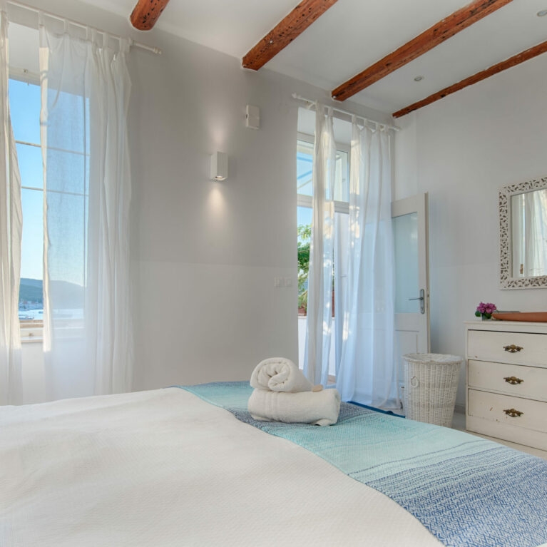 An elegant corner with vintage-inspired furnishings and modern simplicity. Carved wooden accents and light curtains frame a serene and functional space.