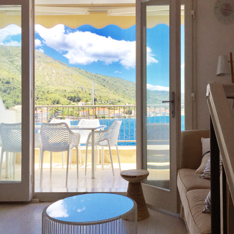 Bright and airy living space seamlessly opens onto a terrace with breathtaking waterfront views. Modern furniture, light tones, and natural elements create a welcoming coastal vibe.