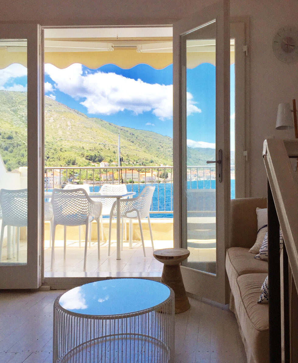 Bright and airy living space seamlessly opens onto a terrace with breathtaking waterfront views. Modern furniture, light tones, and natural elements create a welcoming coastal vibe.