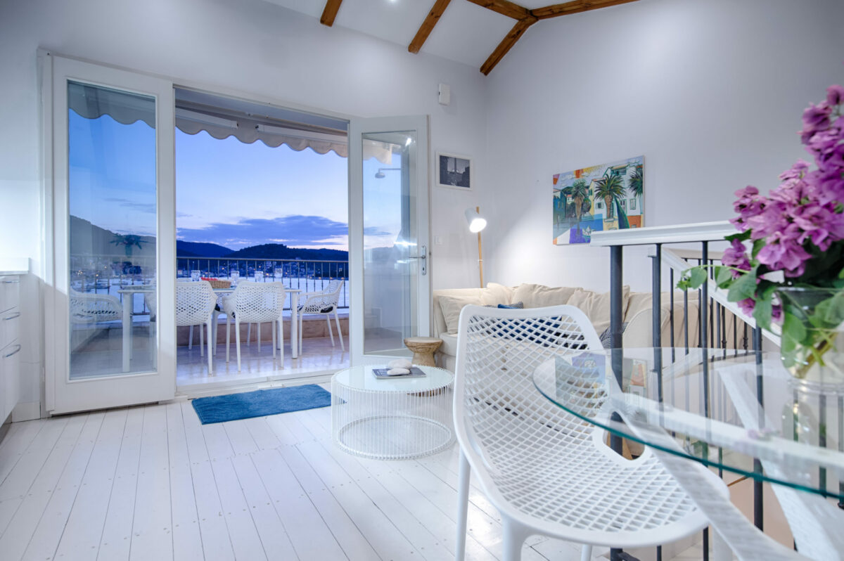 Bright and airy living space seamlessly opens onto a terrace with breathtaking waterfront views. Modern furniture, light tones, and natural elements create a welcoming coastal vibe.