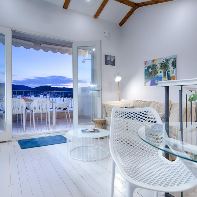 Bright and airy living space seamlessly opens onto a terrace with breathtaking waterfront views. Modern furniture, light tones, and natural elements create a welcoming coastal vibe.