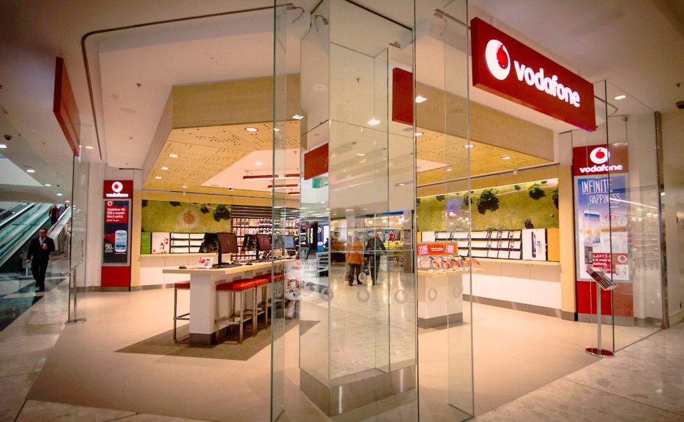 A Vodafone store within a bustling shopping mall, featuring a glass storefront and contemporary, open-plan design.