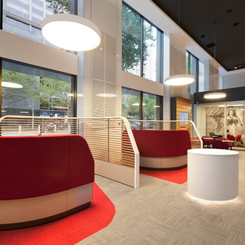 Bank customer lounge, red upholstered booths, curved partition screen, halo pendant lighting, circular plinth, double height curtain wall, commercial carpet tile.